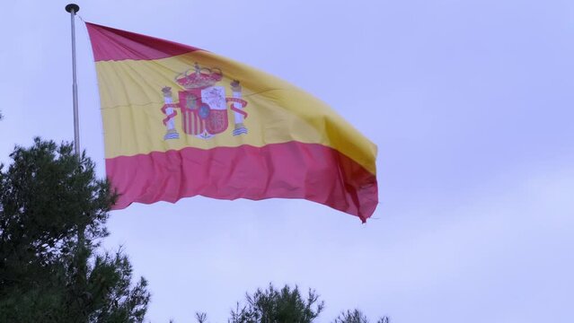 silk national flag with coat arms European state of Spain, flutters in wind in blue sky, concept of tourism, economy, politics, independence day, rights and freedoms of citizens, fair elections