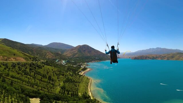 back view from gopro man paraglider flying over the Amirsoy ski slope and Charvak lake in Uzbekistan spreading arms to the sides. Extreme and active types of recreation. High quality FullHD footage