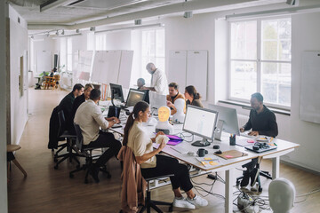 Professors discussing with PhD students over computer at desk in innovation lab