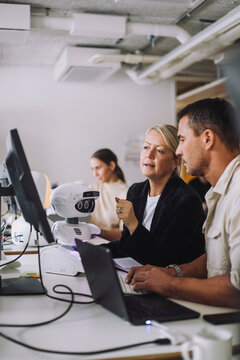 Female mature professor explaining PhD student over computer in innovation lab