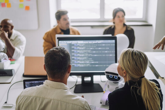 Rear view of professor discussing with student over computer at desk in innovation lab
