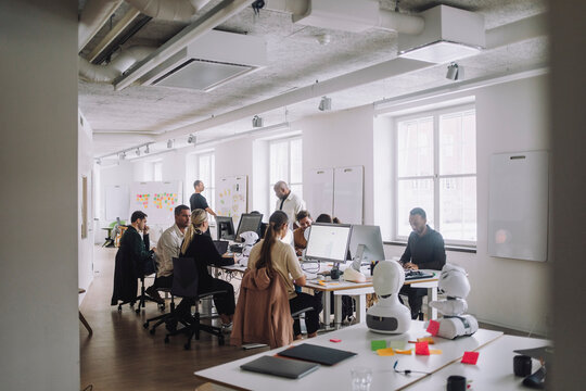 Multiracial professors and PhD students discussing over computer at desk in innovation lab