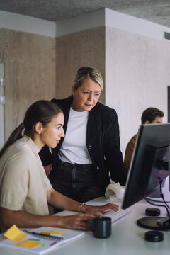 Female professor explaining PhD student over computer at desk in innovation lab