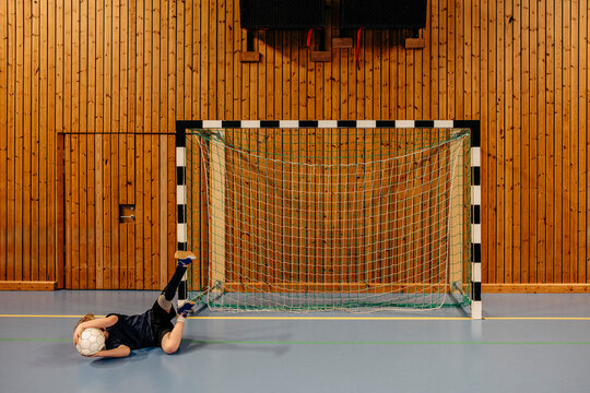 Male goalie with disabled leg lying on floor holding football while playing at sports court - Powered by Adobe