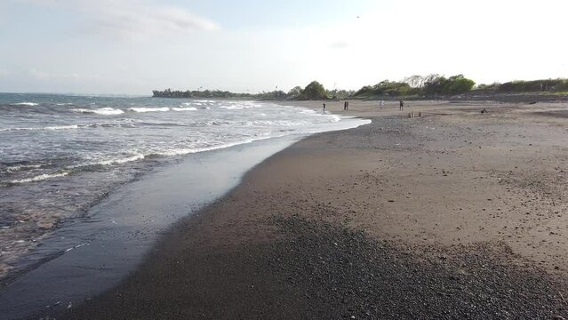 Panoramic Hand Held Shot of Volcanic Black Sand Beach Shore Coastline of Bali Indonesia during Daylight, Waves reaching the Shore