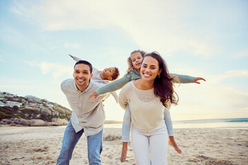 Beach, piggyback and portrait of parents and children for family holiday, summer vacation and weekend. Nature, travel and happy mom, dad and kids playing by ocean for bonding, fun and quality time