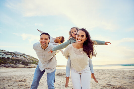 Beach, piggyback and portrait of parents and children for family holiday, summer vacation and weekend. Nature, travel and happy mom, dad and kids playing by ocean for bonding, fun and quality time