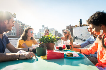 Multiethnic group of young happy friends bonding and having party at home on a rooftop terrace with...