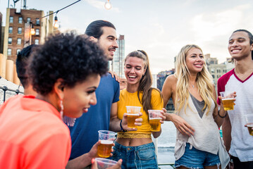 Multiethnic group of young happy friends bonding and having party at home on a rooftop terrace with New York city view
