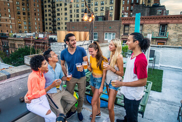 Multiethnic group of young happy friends bonding and having party at home on a rooftop terrace with New York city view