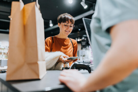Smiling mature woman making payment through smart phone at checkout counter in electronics store
