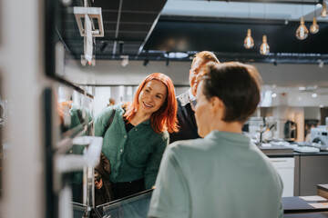 Happy couple looking at microwave oven while saleswoman assisting at electronics store