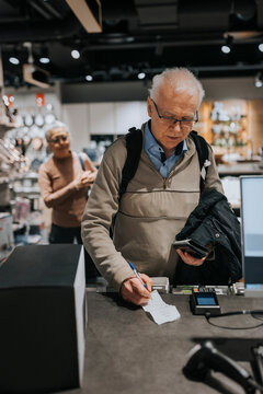 Senior man signing bill by credit card reader at checkout counter in appliances store