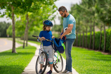 Obraz premium Father and son concept. Father teaching son riding bike. Father helping son to ride a bicycle in american neighborhood. Child in safety helmet learning to ride cycle with his dad. Fathers day.