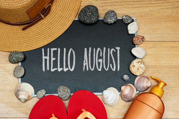 summer concept, sun cream and slipper with hello August text on chalkboard and stones. seashell hat on wood table