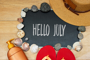 summer concept, sun cream and slipper with hello July text on chalkboard and stones. seashell hat on wood table