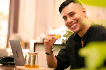Side view of cheerful young man making video call on laptop computer in coffee shop, talking to friends, family and business partners or video communicating with people online