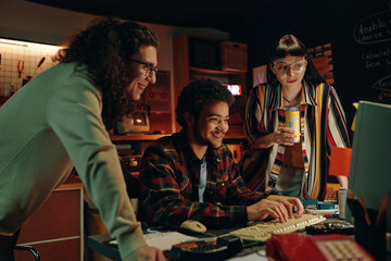 Young guy typing new codes for program on computer with his friends watching for the process during...