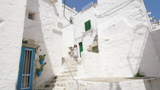 A young girl walks down the stairs in the alley of the white city of Ostuni in the Puglia region of Italy. Turiska walks through a historic city in Europe