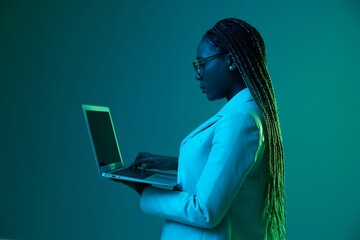 African African woman with laptop in glasses on a blue background in neon light, color mixed light....