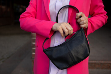 Woman no face. Looking for her phone or handbag in her trendy fashionable black leather bag. Pink...