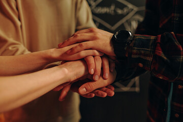 Close-up of team of young people holding hands and supporting each other during their business project