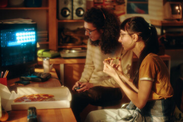 Teenage boy playing video game while girl eating pizza and watching for the game