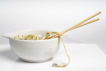 Measuring tape and chopsticks in a white bowl. Weight control concept
