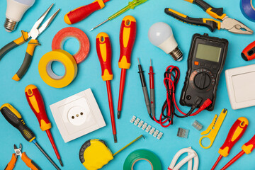 Electrician equipment on blue background with copy space.Top view.Electrician tool set.Multimeter, tester,screwdrivers,cutters,duct tape,lamps,tape measure and wires.Flet lay. © Avocado_studio