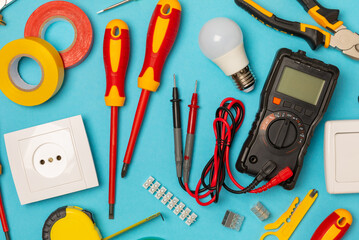 Electrician equipment on blue background with copy space.Top view.Electrician tool set.Multimeter, tester,screwdrivers,cutters,duct tape,lamps,tape measure and wires.Flet lay. © Avocado_studio