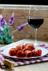 Plate with sliced prosciutto and a glass of red wine on kitchen table, lifestyle photography. Prsut and red wine, italian or spanish cured meats. Jamon appetizer with a glass of wine, brunch concept