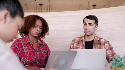Group of multiethnic teenagers studying in private group with Caucasian teacher in modern co-working space, cheerful Asian and African students use technology laptop learning in homeschool class