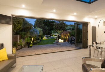 View through open bifold doors of attractive garden on a summer evening with lighting.
