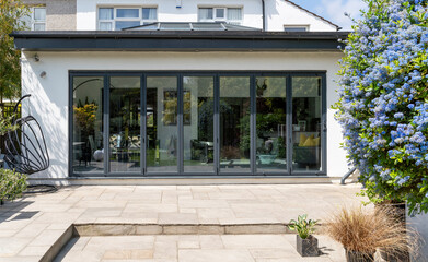 Stylish, closed, bifold doors with plants in spring, summer, revealing interior of a designer, lifestyle, kitchen diner room. - obrazy, fototapety, plakaty
