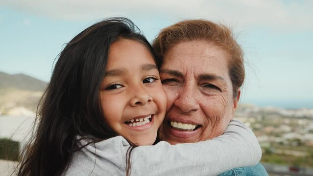 Happy Hispanic child enjoying time with grandmother smiling in front of camera at house rooftop