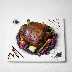 Fried meat on bone with garnish and salad. Dish on white plate with blue cabbage salad is decorated with sauce. Mutton, lamb. White background. View from above. Copy space. 