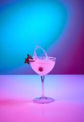 Tasty Margarita glass over pink gradient background in neon glow. Party club entertainment. Mixed light. Champagne splashes