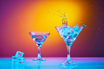 Portrait with glasses of classic dry martini cocktail with olives over colourful gradient background in neon glow. With free space for your text