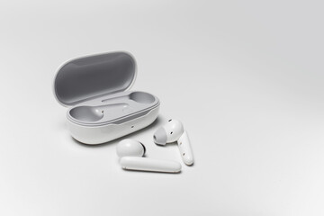 Close-up of white wireless earphones lying near opened charging case on grey background.
