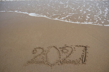 New Year 2027 written in the sand on a beach with sea wave background.