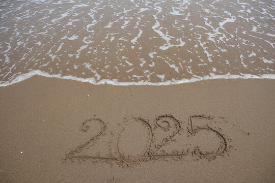 New Year 2025 written in the sand on a beach with sea wave background.