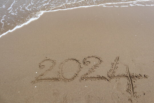 New Year 2024 written in the sand on a beach with sea wave background.