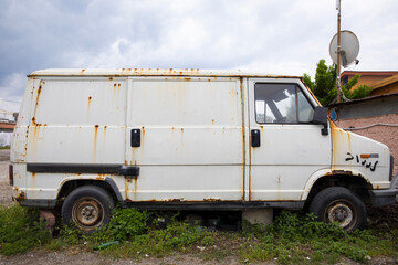 Side view of a very old, rusty, abandoned van. It is off the ground and has long grass underneath. - obrazy, fototapety, plakaty
