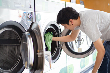 Asian man putting an used or dirty clothes in the self-service automatic laundry washing machine,...