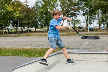 boy enjoys jumping with his push scooter at the skate park