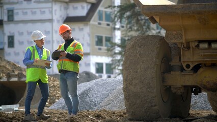 Woman engineer talks on phone with construction site foreman in front of building.