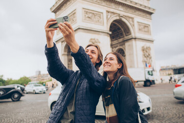 couple taking a selfie in front of the arc de triomphe in paris france