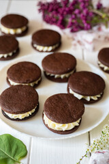 Sweet dessert for children: sweet chocolate chip cookies sandwich with vanilla cream on a white plate on a white background. Vertical photo