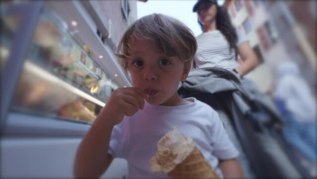 Cute little boy enjoying ice cream cone outside in city street while traveling with family. Child eating gelato