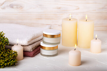 Fototapeta na wymiar Jars with day and night face cream, burning candles, towels and juniper branch on light background. Cosmetic skin care. Concept of calmness, comfort, spa treatments. Selective focus